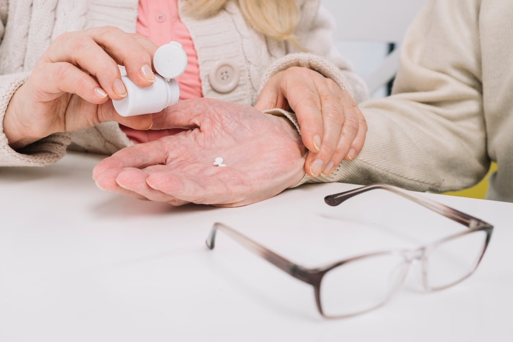 Caregiver pours a single pill into an elderly woman's open hand.